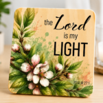 Inspirational wooden coaster featuring Psalm 27:1 scripture, "The Lord is my Light," adorned with delicate cherry blossom flowers, pink buds, and vibrant green leaves. Faith-based Christian coaster with elegant botanical watercolor artwork and natural wood finish, ideal for home décor, Bible study spaces, religious gifts, and inspirational occasions.