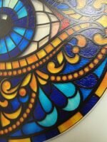 Evil eye acrylic suncatcher with blue, turquoise, orange and gold stained-glass-style design hanging by a window