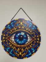 Evil eye acrylic suncatcher with blue, turquoise, orange and gold stained-glass-style design hanging by a window